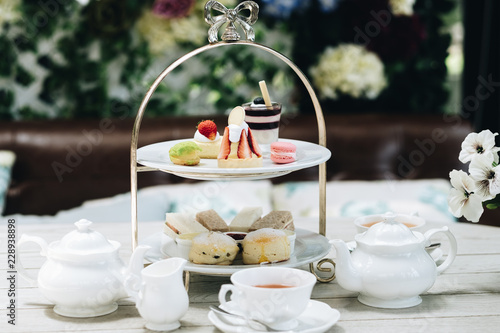 Traditional English afternoon tea: scones with clotted cream and jam, strawberries, with various sandwiches on the background