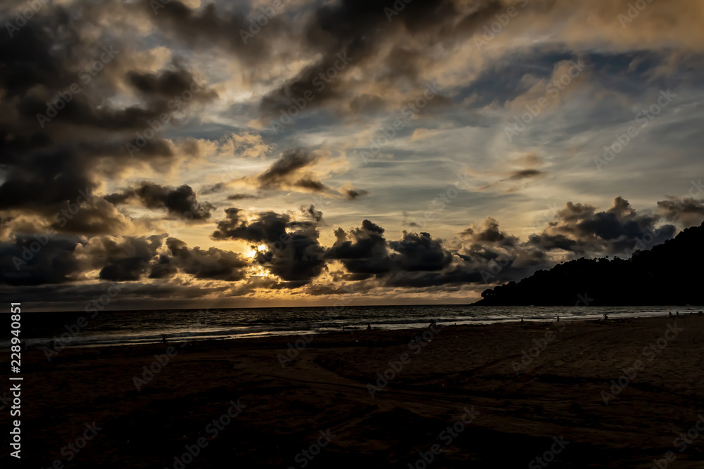 Dramatic clouds over the ocean as the sun sets and the sky turns dark, Karon Beach, Phuket Thailand.