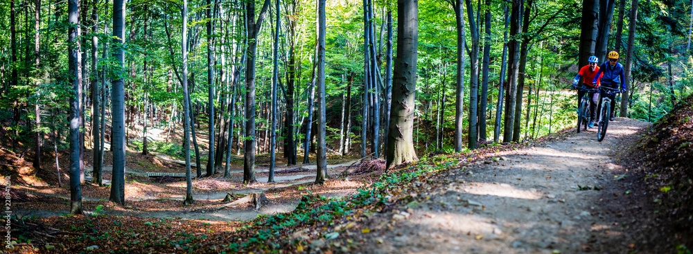 Fototapeta premium Mountain biking women and man riding on bikes in early spring mountains forest landscape. Couple cycling MTB enduro flow trail track. Outdoor sport activity.
