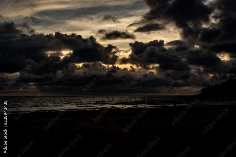 Dramatic clouds over the ocean as the sun sets and the sky turns dark, Karon Beach, Phuket Thailand.