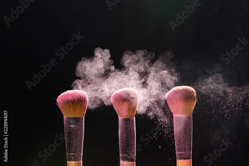 make up, beauty, mineral cosmetic concept - brush brushing away pink powder from another over the black background