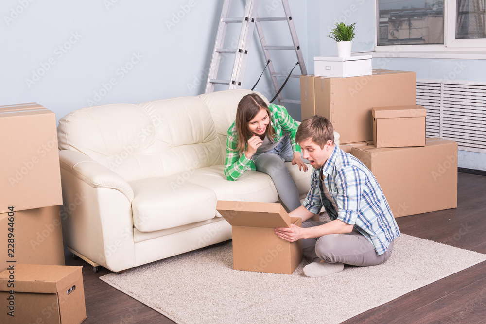 Home, relocation and moving concept - young man looking for something in a box and woman smiling. Home, relocation and moving concept - young man looking for something in a box and woman smiling.