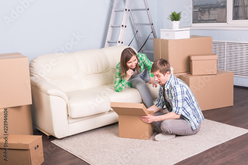 Home, relocation and moving concept - young man looking for something in a box and woman smiling.