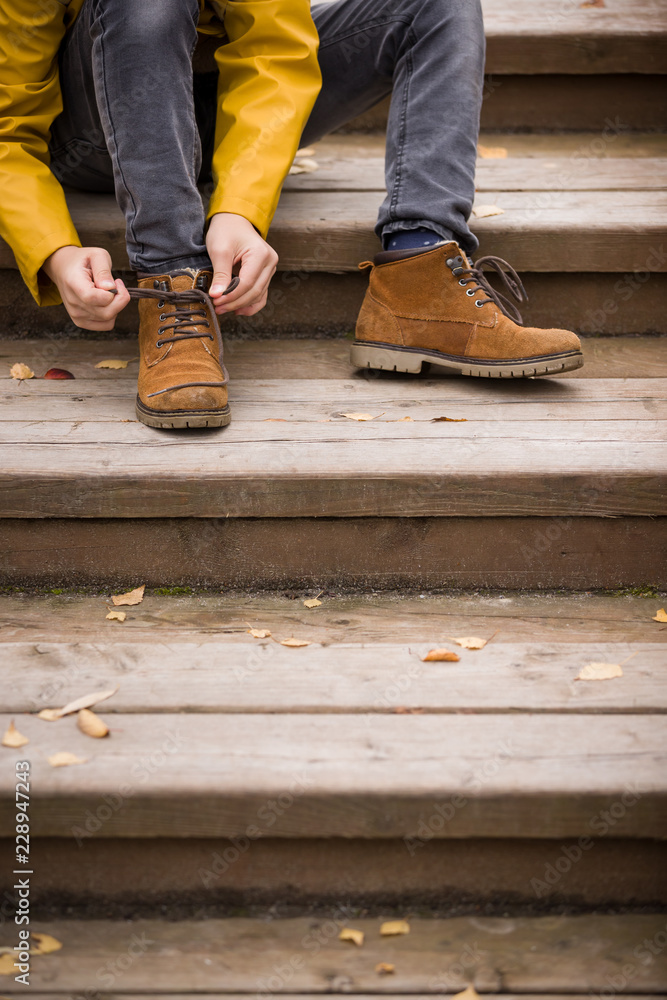 Closeup of child tying laces while walking in the city park. Kid boy on a cold autumn day. - obrazy, fototapety, plakaty 