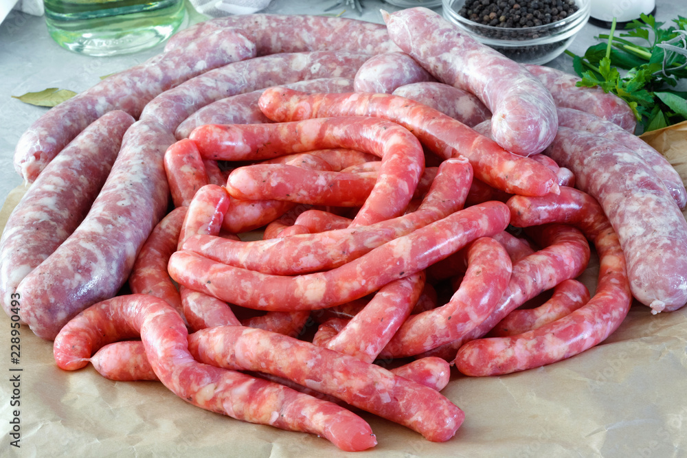 Raw meat sausages in on parchment paper, with bay leaves and fresh herbs in the kitchen. Raw meat sausages in on parchment paper, with bay leaves and fresh herbs in the kitchen.