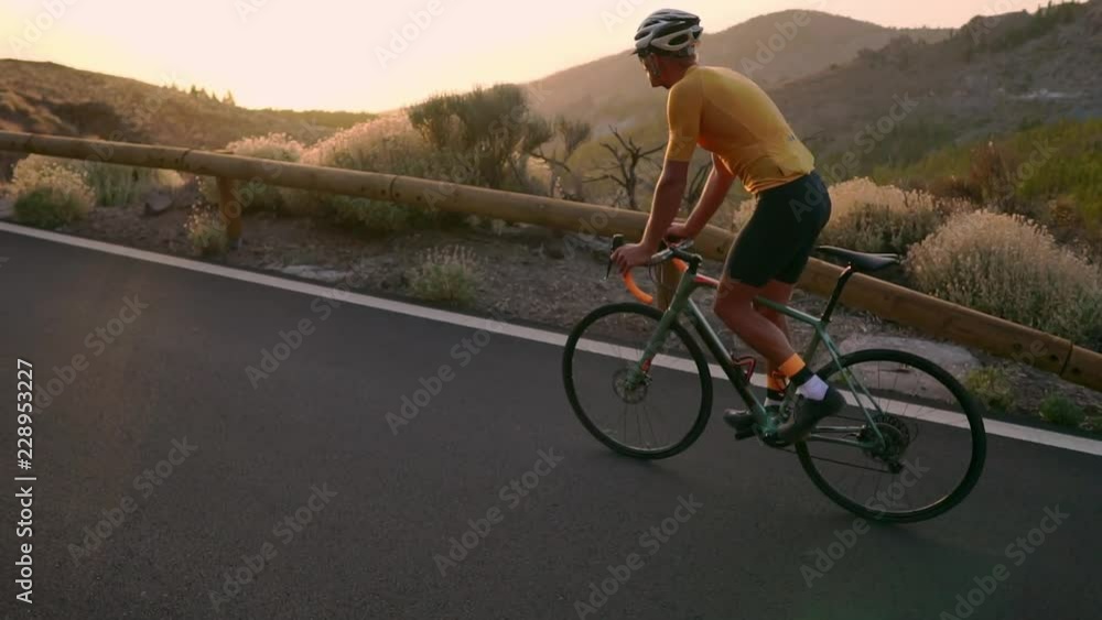 A professional cyclist in a helmet and sports equipment rides on a mountain highway at sunset in slow motion. Steadicam A professional cyclist in a helmet and sports equipment rides on a mountain highway at sunset in slow motion. Steadicam