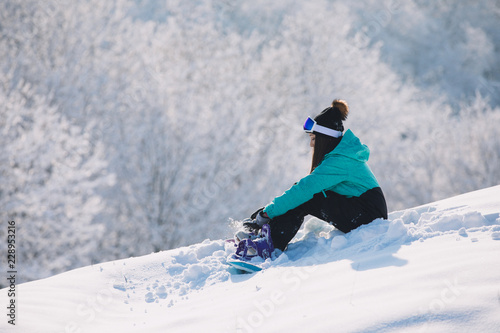 Woman snowboarder sitting on high hill and rest
