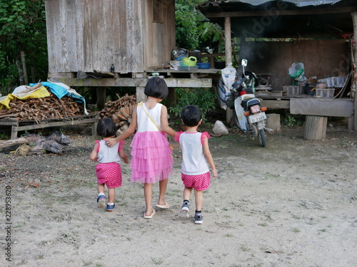 Asian baby girl (middle) taking her two little baby sisters for a walk to a separate kitchen in a rural area of Thailand