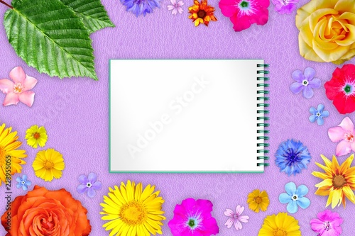 Beautiful flower frame with copybook in center on purple hard leather background. Floral composition of spring or summer flowers.