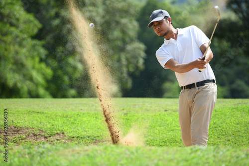 Young Asian man golfer hitting a bunker shot