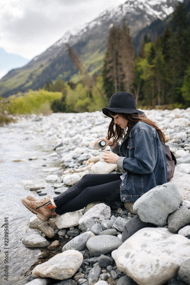 Woman is pouring hot drink from thermos into travel mug