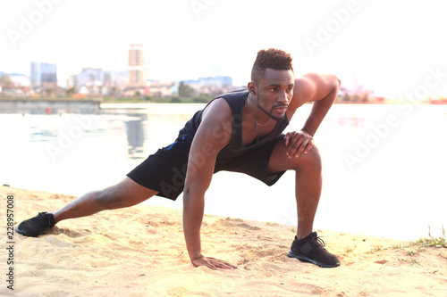 African man in sports clothing warming up, in beach outdoor portrait, at sunset or sunrise.