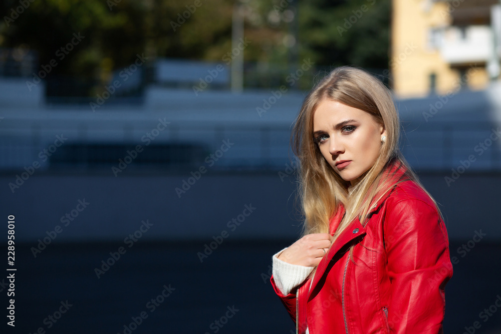 Fashionable young model with long hair wearing leather jacket posing with sun light. Empty space
