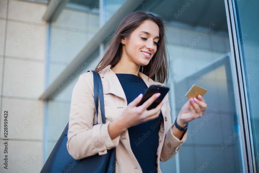 Low Angle Of Pleased Girl Standing at the Airport Hall. He is Using Gold Credit card and Cellphone For Paying Low Angle Of Pleased Girl Standing at the Airport Hall. He is Using Gold Credit card and Cellphone For Paying