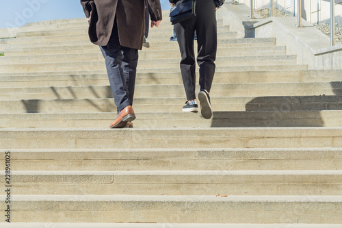 Two people in business casual wear walking upstairs outdoors. Urban background