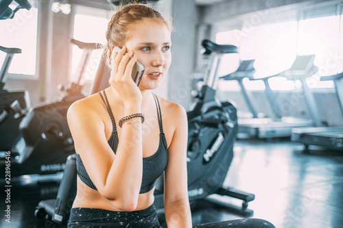 Active girl using smartphone in fitness gym.Young smiling woman at the gym relaxing and listening to music using a mobile phone