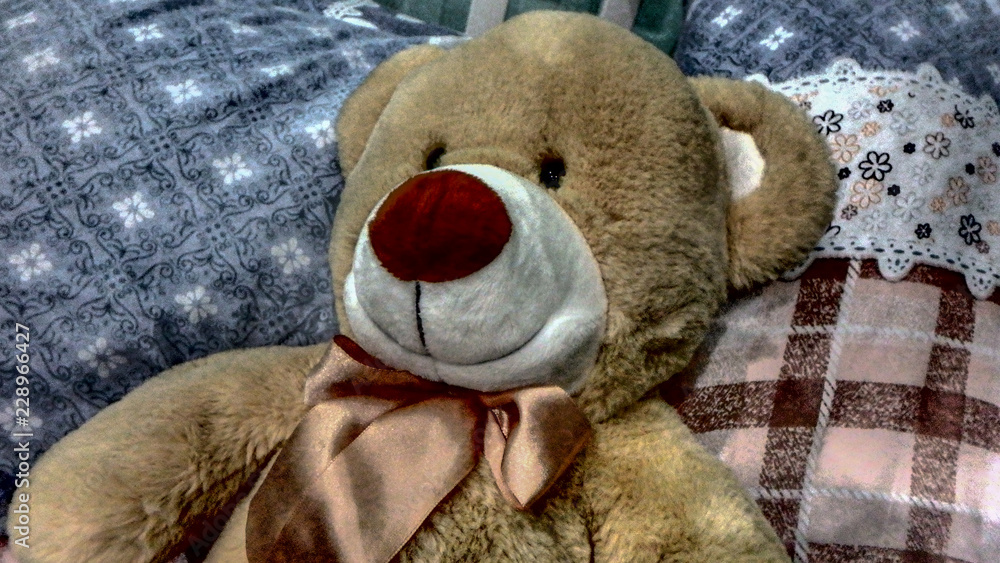 A plush teddy bear sitting on a bed with a quilted pattern.