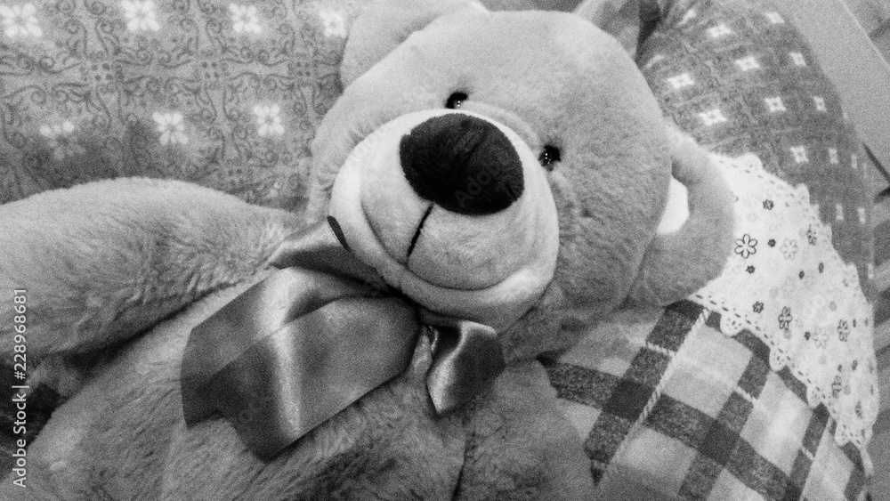 A plush teddy bear sitting on a bed with a quilted pattern.