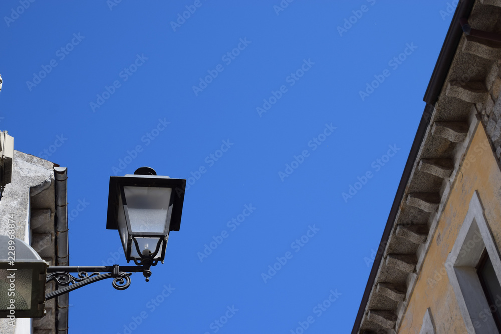 decorative and nostalgic street lamp in front of azure sky, vintage iron street lantern on a house facade decorative and nostalgic street lamp in front of azure sky, vintage iron street lantern on a house facade