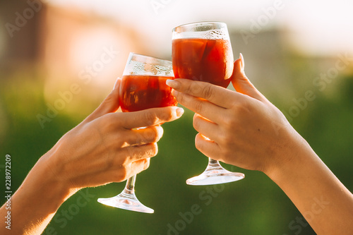 Cheers. Female hands cheering on sunset with red wine fresh sangria glasses with green sunny garden background - female friendship, holidays celebrating and party concept photo