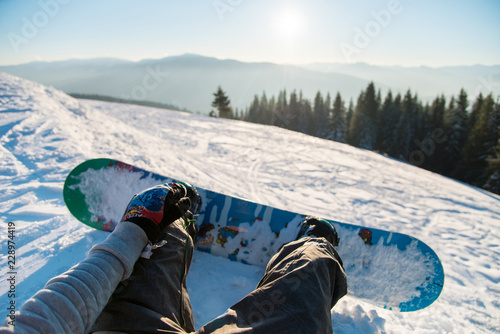 Point of view shot of a female snowboarder lying on the snow on the slope relaxing after riding, enjoying stunning view of winter mountains and sunset POV concept photo