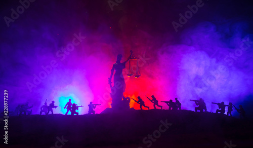 War - no justice concept. Military silhouettes fighting scene and The Statue of Justice on a dark toned foggy background. © zef art