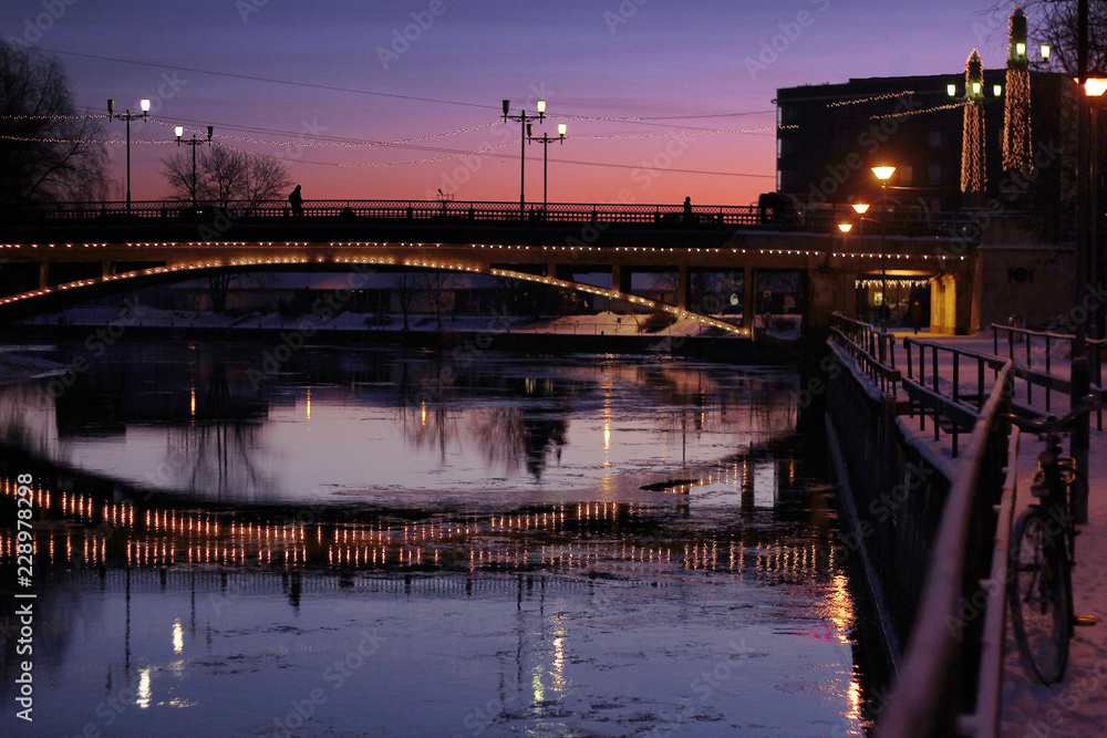 sunset scene in winter town with a bridge over a river and a parked bicycle