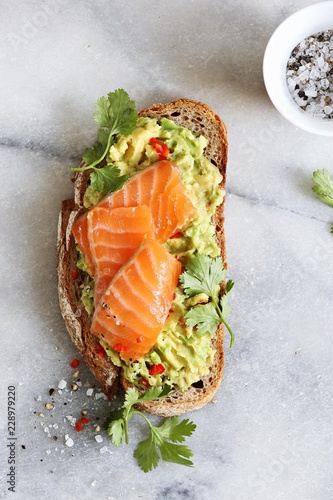 Smashed avocado and smoked salmon on rye bread. Sandwich with gravlax and avocado overhead marble table. photo