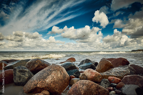 Stones at the beach with wave and nice blue sky with clouds