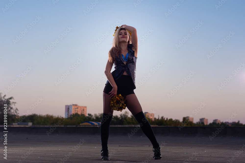cheerleader with pompoms dancing outdoors on the roof at sunset