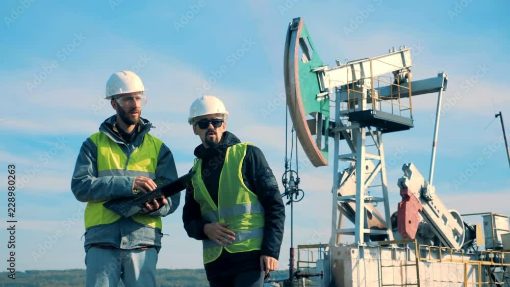 Men in uniform working on an oilfield near towers. Oil industry concept. Men in uniform working on an oilfield near towers. Oil industry concept.