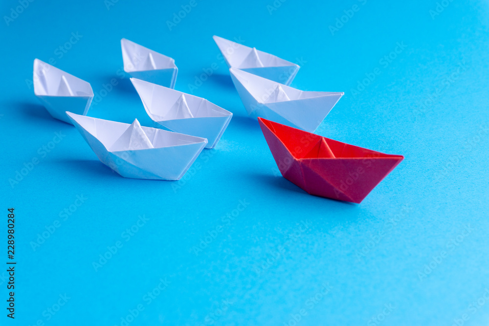 White and red paper ship in one direction on blue background. Business for innovative solution concept with selective focus White and red paper ship in one direction on blue background. Business for innovative solution concept with selective focus