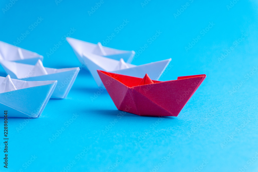 White and red paper ship in one direction on blue background. Business for innovative solution concept with selective focus White and red paper ship in one direction on blue background. Business for innovative solution concept with selective focus