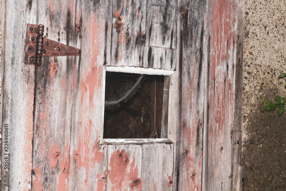 Close up of an old wooden shack door with a square window and peeling red paint.
