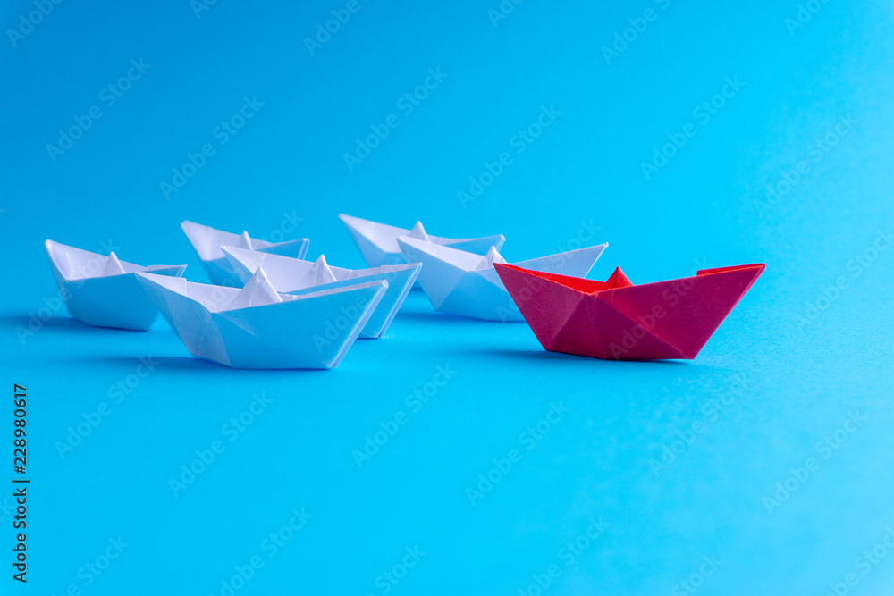 White and red paper ship in one direction on blue background. Business for innovative solution concept with selective focus