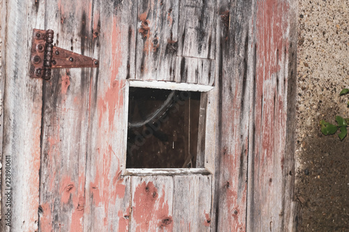 Obraz na płótnie Close up of an old wooden shack door with a square window and peeling red paint. w salonie