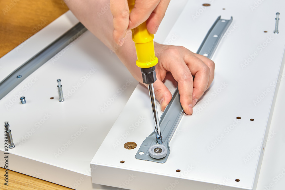 Repairman is screwing screw in drawer slide bracket using screwdriver. Repairman is screwing screw in drawer slide bracket using screwdriver.