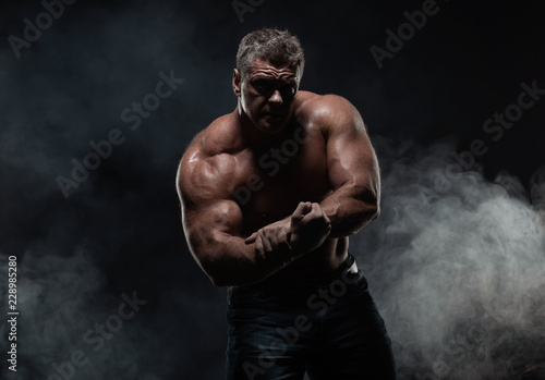 powerful muscular man shows biceps on a black background. Strength and fitness concept
