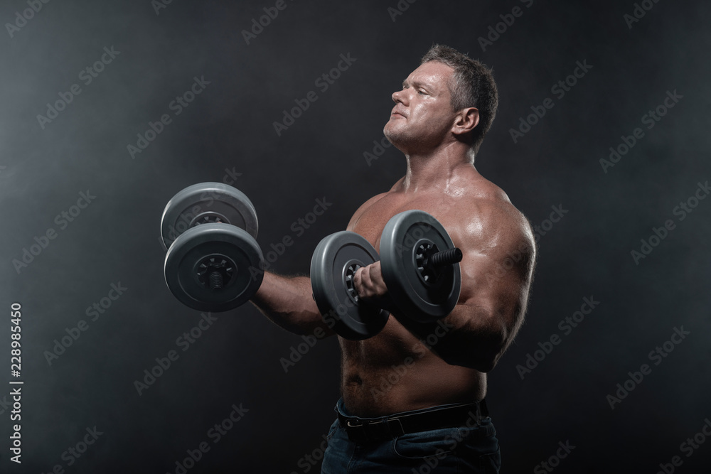 muscular man trains with dumbbells on black background in smoke