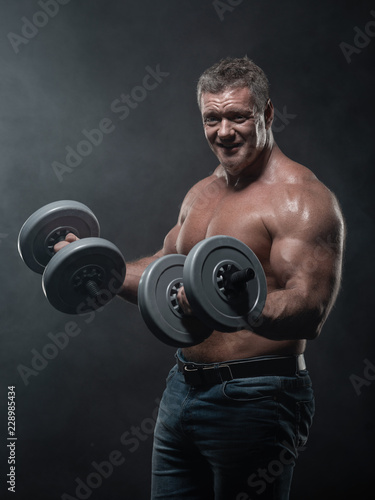 muscular man trains with dumbbells on black background in smoke © Vladimir
