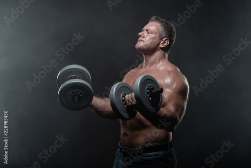 muscular man trains with dumbbells on black background in smoke © Vladimir