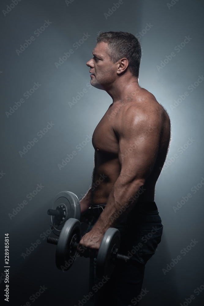 muscular man trains with dumbbells on black background in smoke