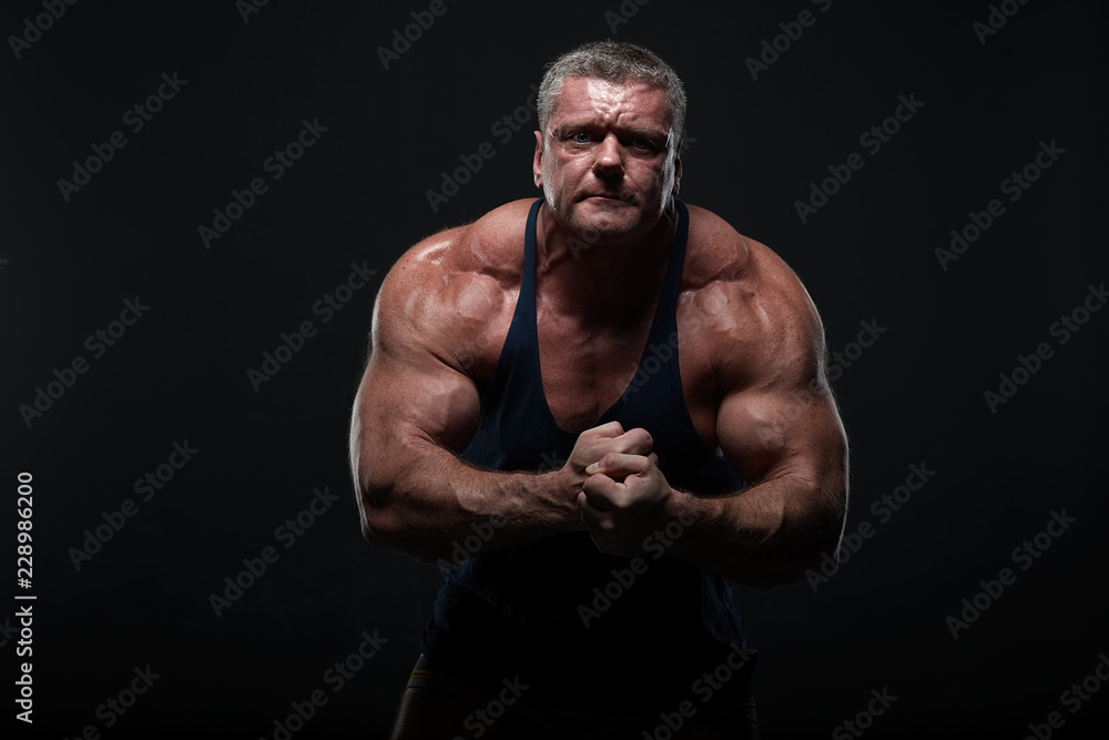 powerful muscular man shows biceps on a black background. Strength and fitness concept