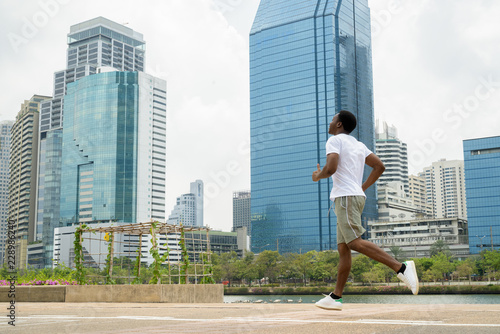 Young African man running outdoors in park with cityscape
