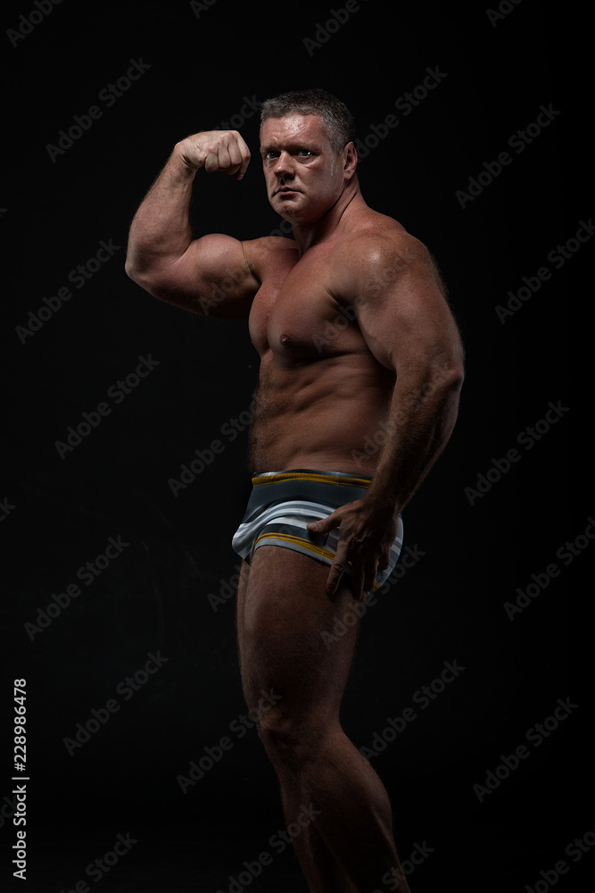 Powerful muscular bodybuilder posing on a black background. concept of strength and health