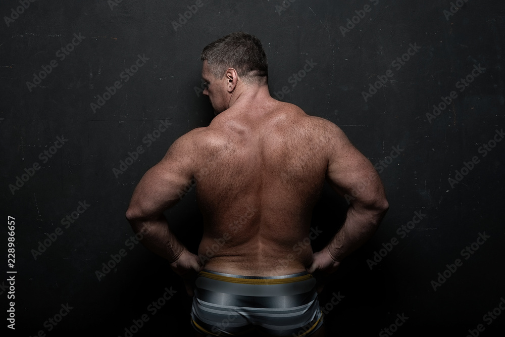 powerful muscular athlete shows off his back near a black grunge wall