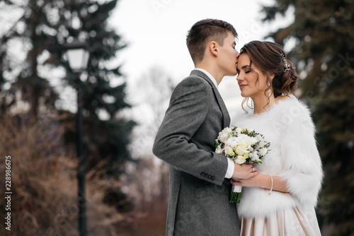 Winter fairy tale. Loving and beautiful bride and groom stand in the winter forest