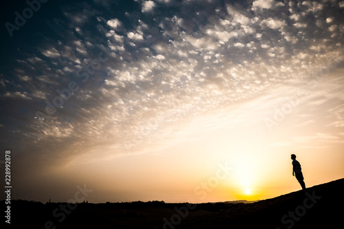 Man in black silhouette standing on the ground during a warm yellow coloured sunset. clouds and sun in background. emotion and feeling concept for people enjoy the outdoors lifestyle