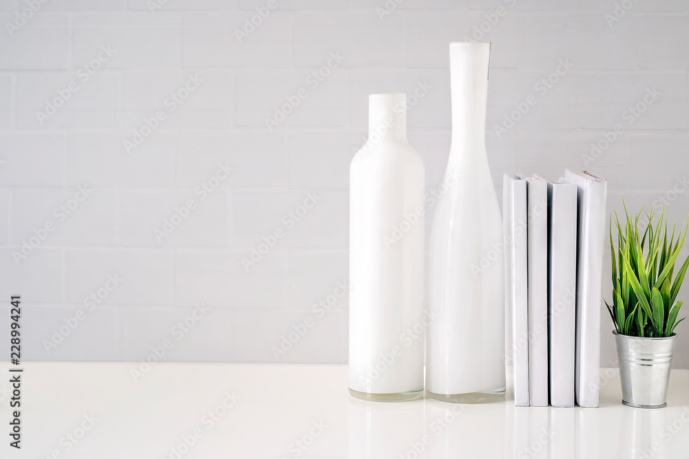 Mock up glass bottle, books and houseplant on white table with white brick wall