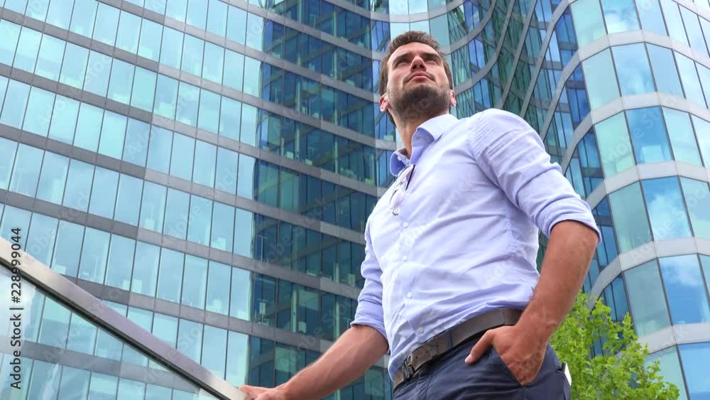 A businessman stands in front of an office building and looks around proudly - closeup from below A businessman stands in front of an office building and looks around proudly - closeup from below